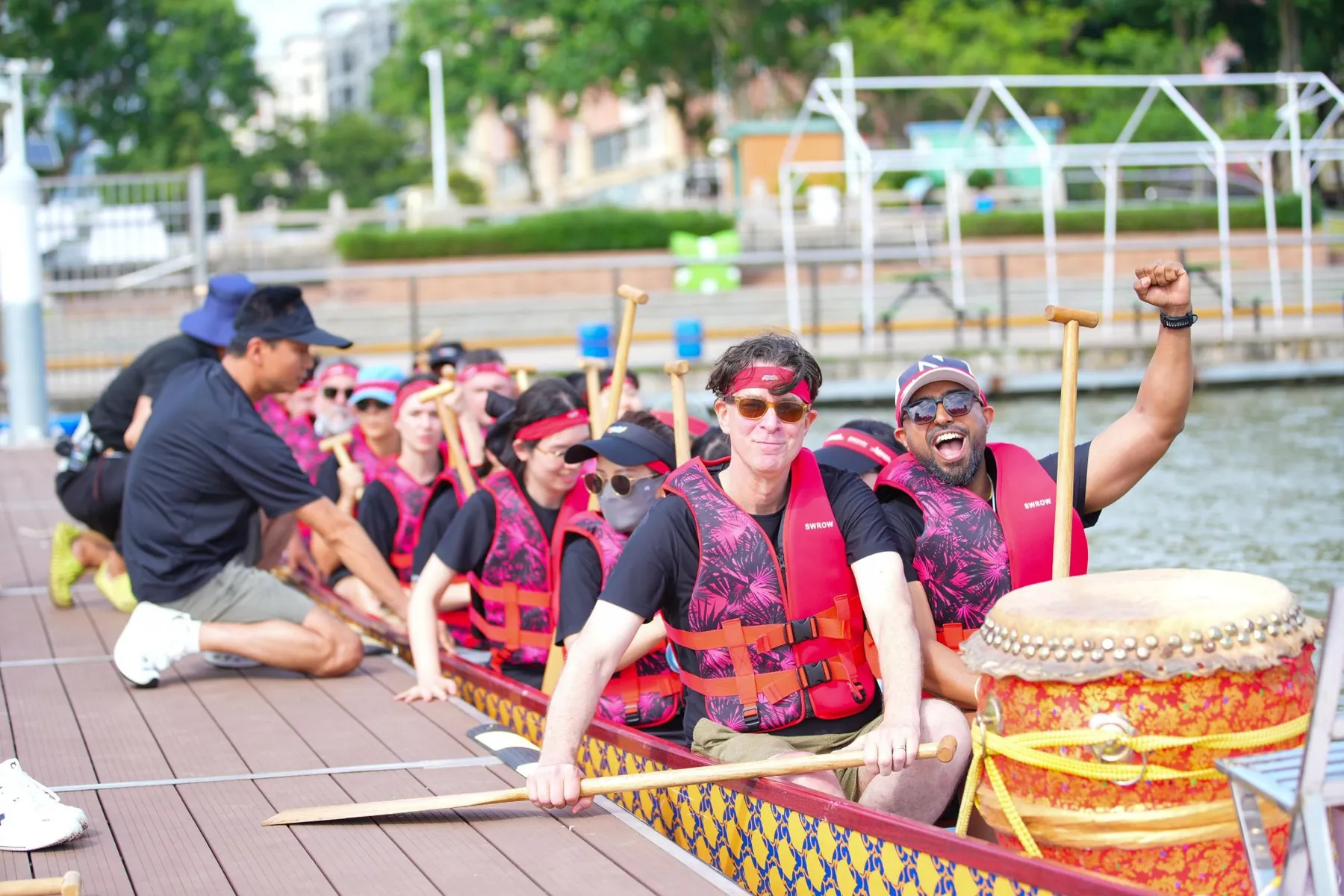 Dhee in a dragon boat in a life vest, fist in the air, shouting with joy.